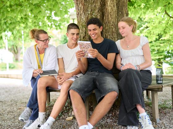 Schüler unterschiedlicher Nationalitäten mit Lehrerin unter einem Baum